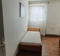 Einzelbett im Zimmer mit Fenster und Vorhang in einer Zweizimmerwohnung.