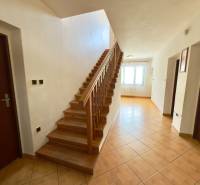 Innenraum eines Einfamilienhauses mit einer Holztreppe, einem gefliesten Flur und einem Fenster, das den Raum erhellt.