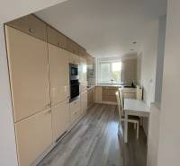 Küche in einer 2-Zimmer-Wohnung mit weißen Möbeln und Holzboden.