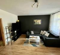 Wohnzimmer in einer Zweizimmerwohnung mit Sofa, Tisch und schwarzer Wand.