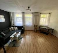 Wohnzimmer mit schwarzem Sofa, weißem Tisch und Schreibtisch in einer Zweizimmerwohnung.