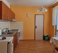 Eine Küche in einer 2-Zimmer-Wohnung mit orangefarbenen Wänden, Holzboden und einem Esstisch.