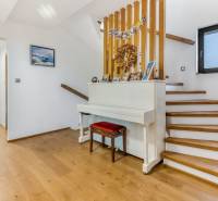 Innenraum eines Einfamilienhauses mit Treppe, weißem Klavier und Holzboden.