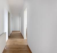 Der Flur in einer 3-Zimmer-Wohnung mit weißen Wänden und Holzboden.
