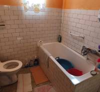 Badezimmer in einem Einfamilienhaus mit weißen Fliesen, Badewanne und Toilette.