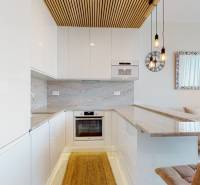 Küche in einer 2-Zimmer-Wohnung mit weißen Schränken, Ziegeldetails und Naturstein.