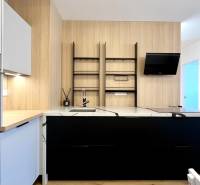 Küche in einer 2-Zimmer-Wohnung mit weißen und schwarzen Schränken, eingebautem Ofen und Holzelementen.