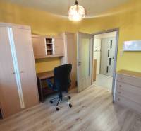 Ein Zimmer mit Möbeln in einer 3-Zimmer-Wohnung, Holzboden, gelbe Wände, Schreibtisch, Stuhl.