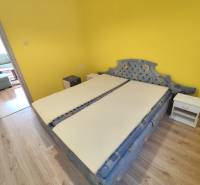 Schlafzimmer in einer 3-Zimmer-Wohnung mit gelber Wand, Bett und Nachttischen.