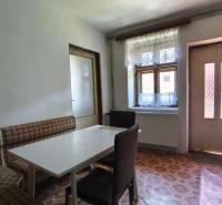Innenraum eines Einfamilienhauses mit Tisch, Stühlen und Sitzbank, einfache Küche.