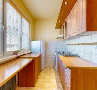 Küche in einer 3-Zimmer-Wohnung mit Holzschränken, Arbeitsplatte und großen Fenstern mit Vorhängen.