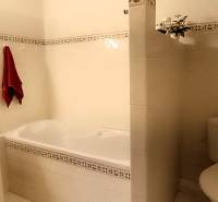 Badezimmer mit Badewanne und Waschbecken in einer 3-Zimmer-Wohnung, helle Fliesen, rotes Handtuch.