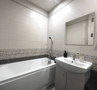 Badezimmer in einer 2-Zimmer-Wohnung mit Badewanne, Waschbecken und Spiegel an der Wand.