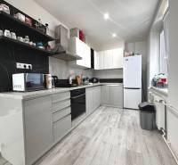 Küche in einer 2-Zimmer-Wohnung mit weißen Möbeln, Geräten und schwarzem Fliesenspiegel.