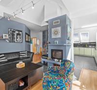 Wohnzimmer in einem Einfamilienhaus mit Sofa, Kamin, dekorativen Bildern und Küche.