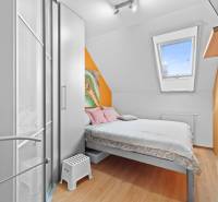 Kleines Schlafzimmer in einem Einfamilienhaus mit Bett, Schrank und bunten Wänden.