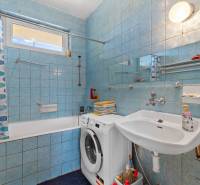 Badezimmer mit Waschbecken, Badewanne und Waschmaschine in einem Einfamilienhaus. Blaue Fliesen und Duschvorhang.