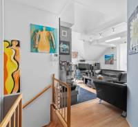 Wohnzimmer mit Kunstgemälden, schwarzen Ledersofas und einer Holztreppe in einem Einfamilienhaus.