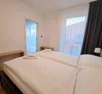 Schlafzimmer in einer Zweizimmerwohnung mit zwei Betten, Holztischen und Vorhängen.