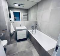 Badezimmer mit Badewanne, Waschbecken und Spiegel in einer 2-Zimmer-Wohnung mit Fliesen.