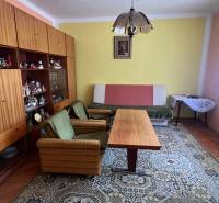 Wohnzimmer in einem Einfamilienhaus mit Retro-Möbeln, grünen Sesseln und einem großen Teppich.