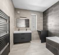 Geräumiges Badezimmer in einer 3-Zimmer-Wohnung mit grauen Fliesen, Doppelwaschbecken und Badewanne.
