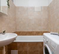 Badezimmer mit Badewanne, Waschbecken und Waschmaschine in einer Einzimmerwohnung.