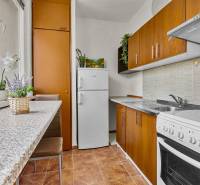Kompakte Küche mit braunen Schränken und weißen Geräten in einer Einzimmerwohnung.