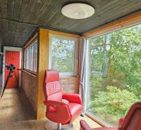 Ein Einfamilienhaus mit verglaster Veranda, roten Sesseln, Teleskop und Blick auf den Wald.