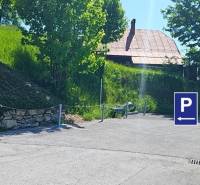 Parkplatz in der Donovaly-Straße in der Stadt Donovaly bei Einfamilienhäusern, mit Bäumen und Gras.