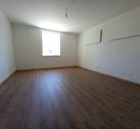 Ein Zimmer mit Holzboden und einem hellen Fenster in einem Einfamilienhaus.