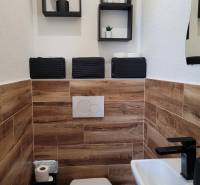 Toilette in einer 3-Zimmer-Wohnung mit Holzverkleidung und schwarzen Accessoires.