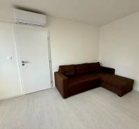 Helles Zimmer mit Ecksofa und Klimaanlage in einer Einzimmerwohnung.