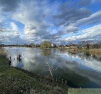 Idyllische Landschaft mit einem See, Wolken und Einfamilienhäusern im Hintergrund am Ufer.