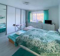 Schlafzimmer im Einfamilienhaus mit großem Bett und grünen Vorhängen, heller Innenraum.
