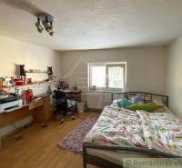 Ein Schlafzimmer in einem Einfamilienhaus mit Bett, Schreibtisch und einfacher Beleuchtung.