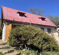Ein Ferienhaus in Rožňava mit rotem Dach, umgeben von üppigem Grün und klarem Himmel.