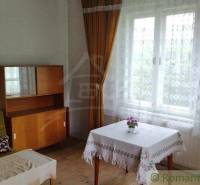 Ein Zimmer in einem Einfamilienhaus mit einer Holzkredenz, einem Sofa und einem Tisch am Fenster.