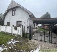 Ein Einfamilienhaus mit weißer Fassade und Tor, umgeben von Rasen und Zaun.