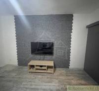 Fernseher an der Steinwand, darunter ein Holztisch, Raum in einem Einfamilienhaus.
