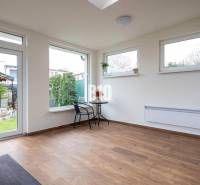Innenraum eines Einfamilienhauses mit Holzboden, Tisch und Stühlen bei großen Fenstern.