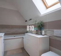 Ein Badezimmer in einem Einfamilienhaus mit einer Badewanne, hellen Fliesen und einem Dachfenster.