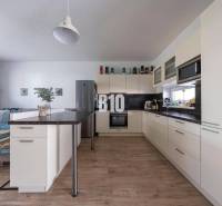 Küche mit Insel und bequemer Sitzgelegenheit in einem Einfamilienhaus, helle Putzwände und Holzboden.
