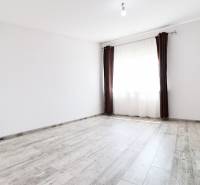 Ein leerer Raum mit weißen Wänden, braunen Vorhängen und Holzboden in einem Einfamilienhaus.