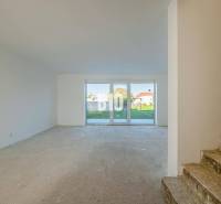 Ein Raum in einem Einfamilienhaus mit großen Fenstern und Betonboden, im Hintergrund eine Treppe.
