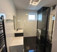 Ein Badezimmer in einem Einfamilienhaus mit schwarzen Böden, weißen Wänden und einer Duschkabine.