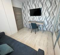 Ein Zimmer in einem Einfamilienhaus mit wellenförmiger Tapete, Fernseher, Sofa und Schreibtisch.