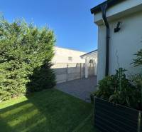 Rasen und gepflasterter Gehweg bei einem Einfamilienhaus in Gabčíkovo mit Sträuchern und klarem Himmel.