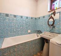 Badezimmer im Einfamilienhaus mit Badewanne, Waschbecken und Waschmaschine, gefliest mit blauen Fliesen.