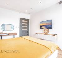 Helles Schlafzimmer in einem Einfamilienhaus mit Fernseher, Spiegel und gelber Bettdecke.